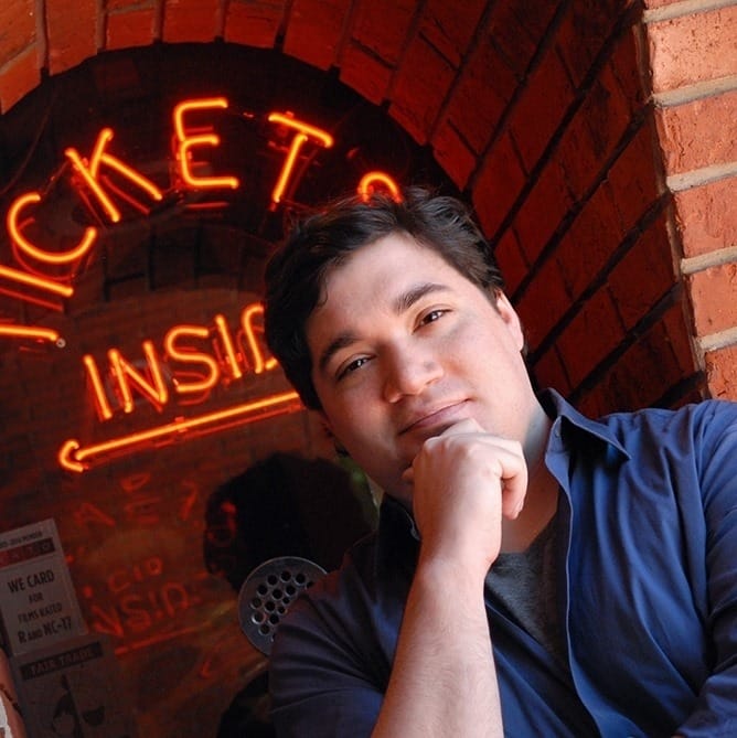 Writer Bill Arceneaux, posing with a contemplative look, in front of the ticket booth for the Prytania Uptown Theatre in New Orleans, LA